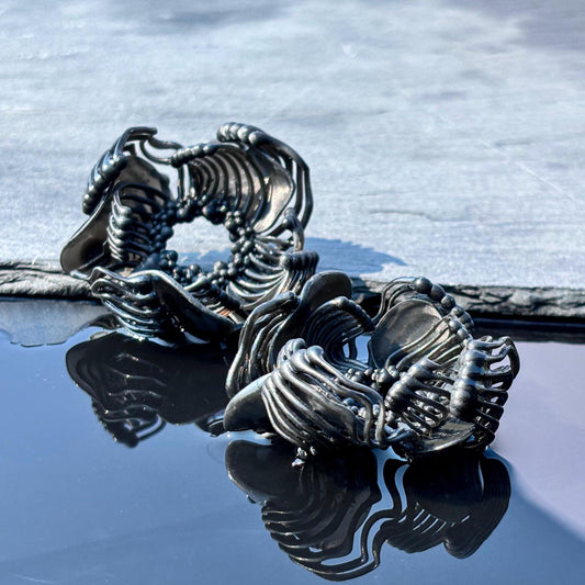 Close-up of black flower earrings, showing the minimalist sculpture and small piece of jewelry detail.