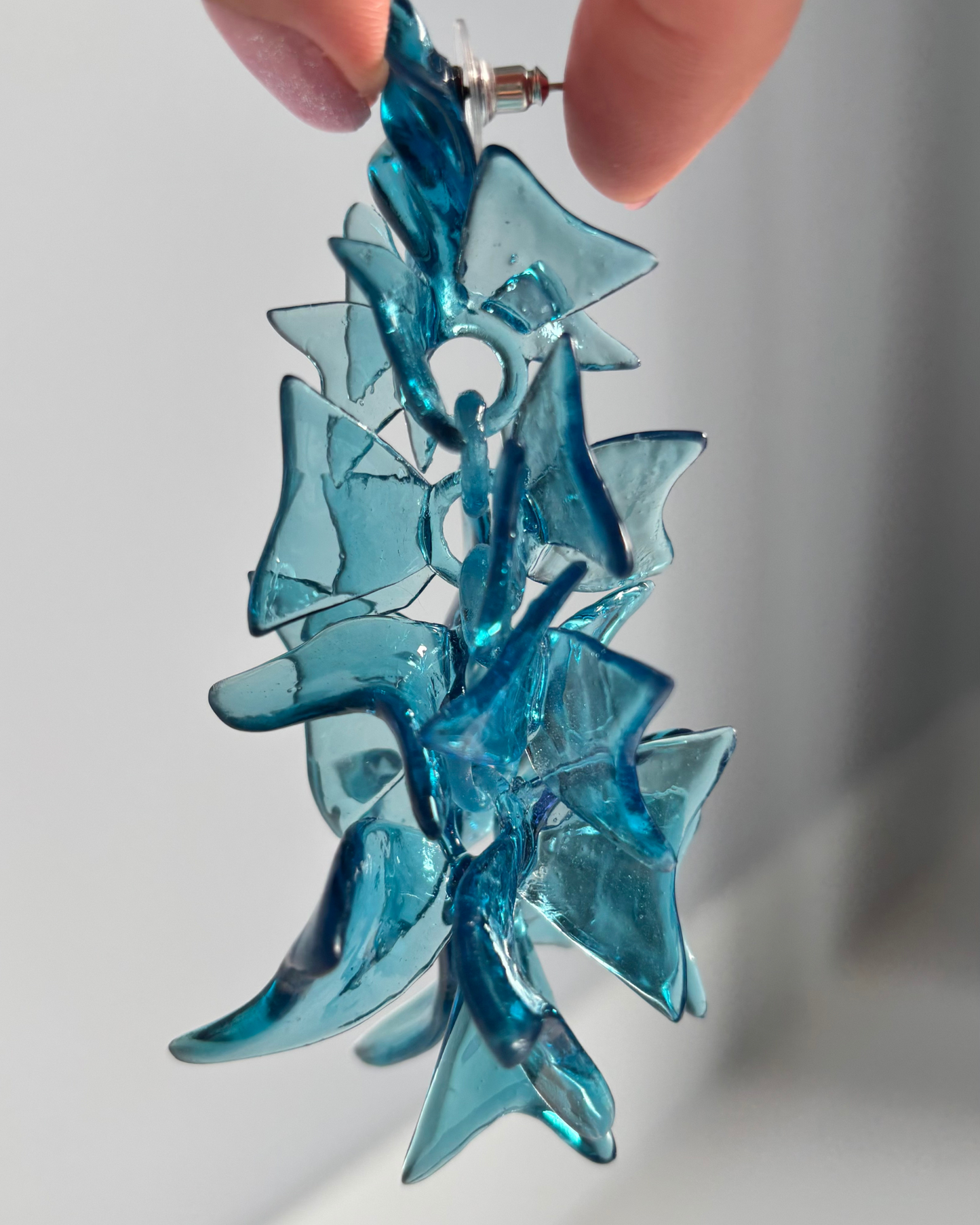 Hand holding the long blue sculptural earring, demonstrating movement