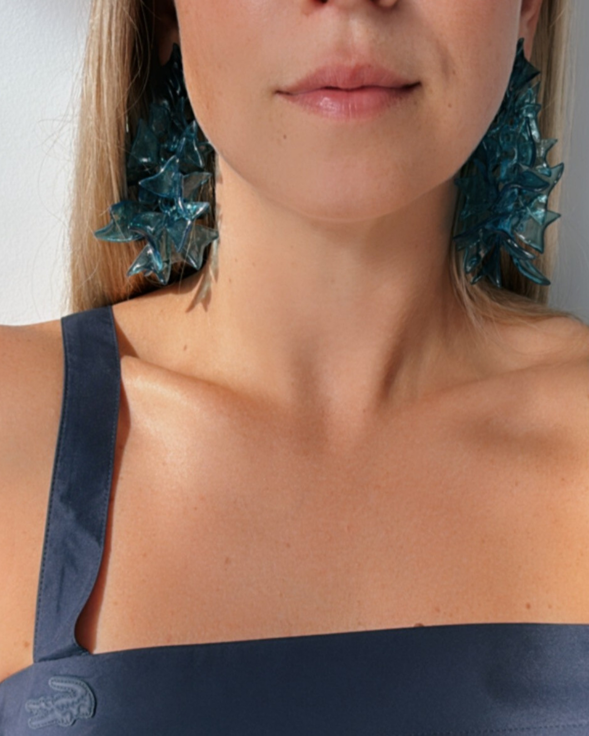 Model wearing blue sculptural earrings, focusing on face and earring lines