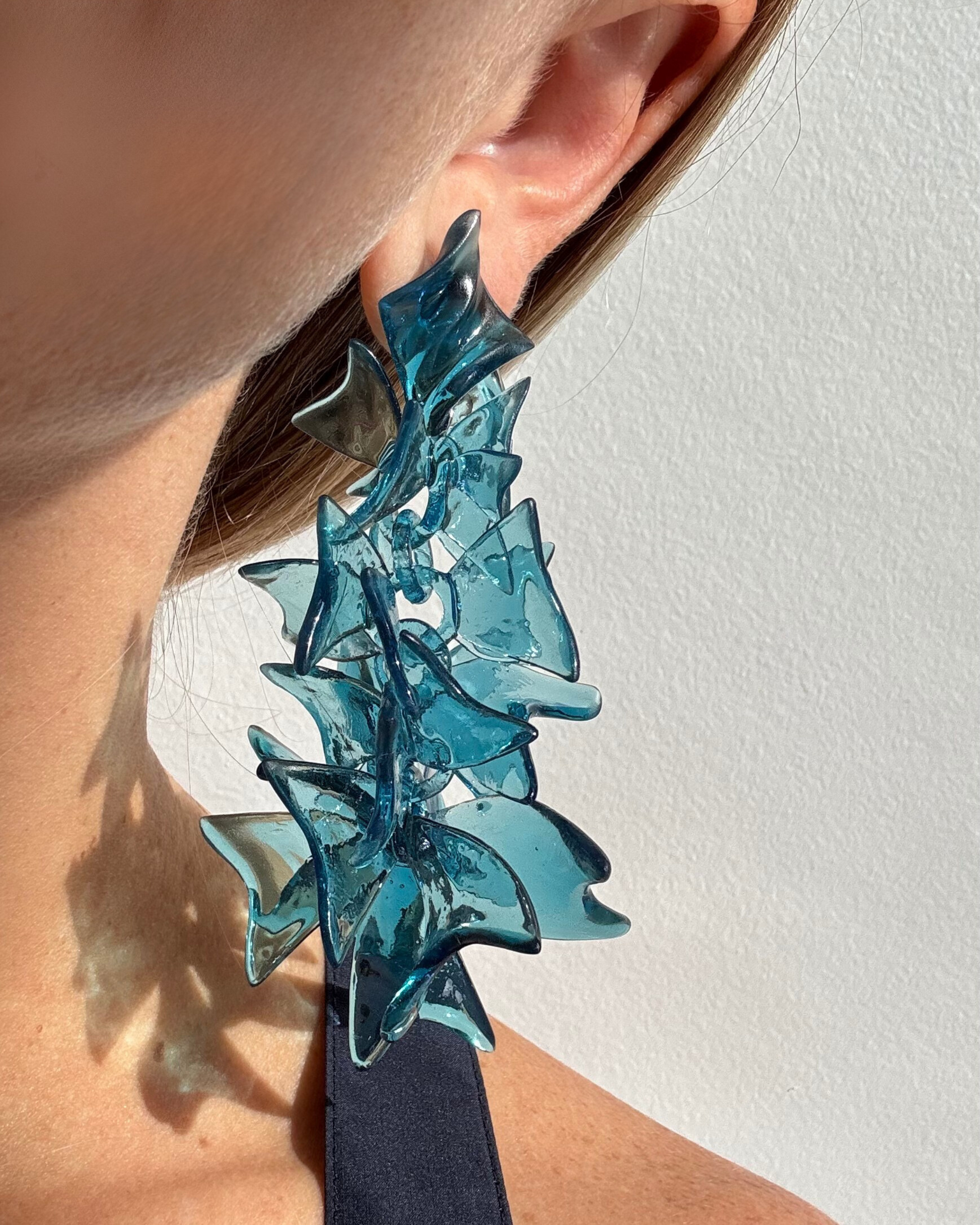 Side profile of model wearing long blue sculptural earrings, left ear visible