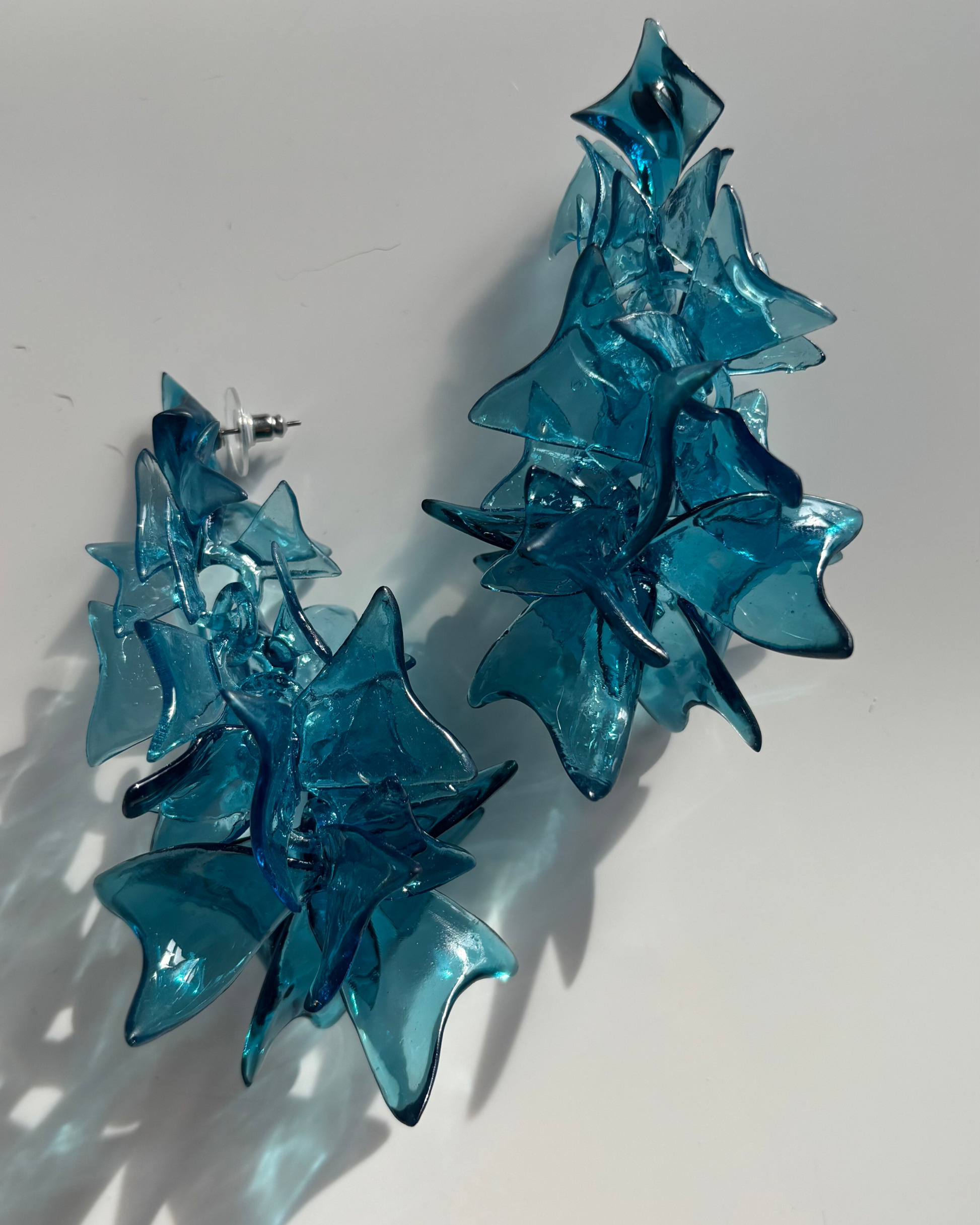 Blue sculptural earrings casting a shadow, highlighting the architectural form