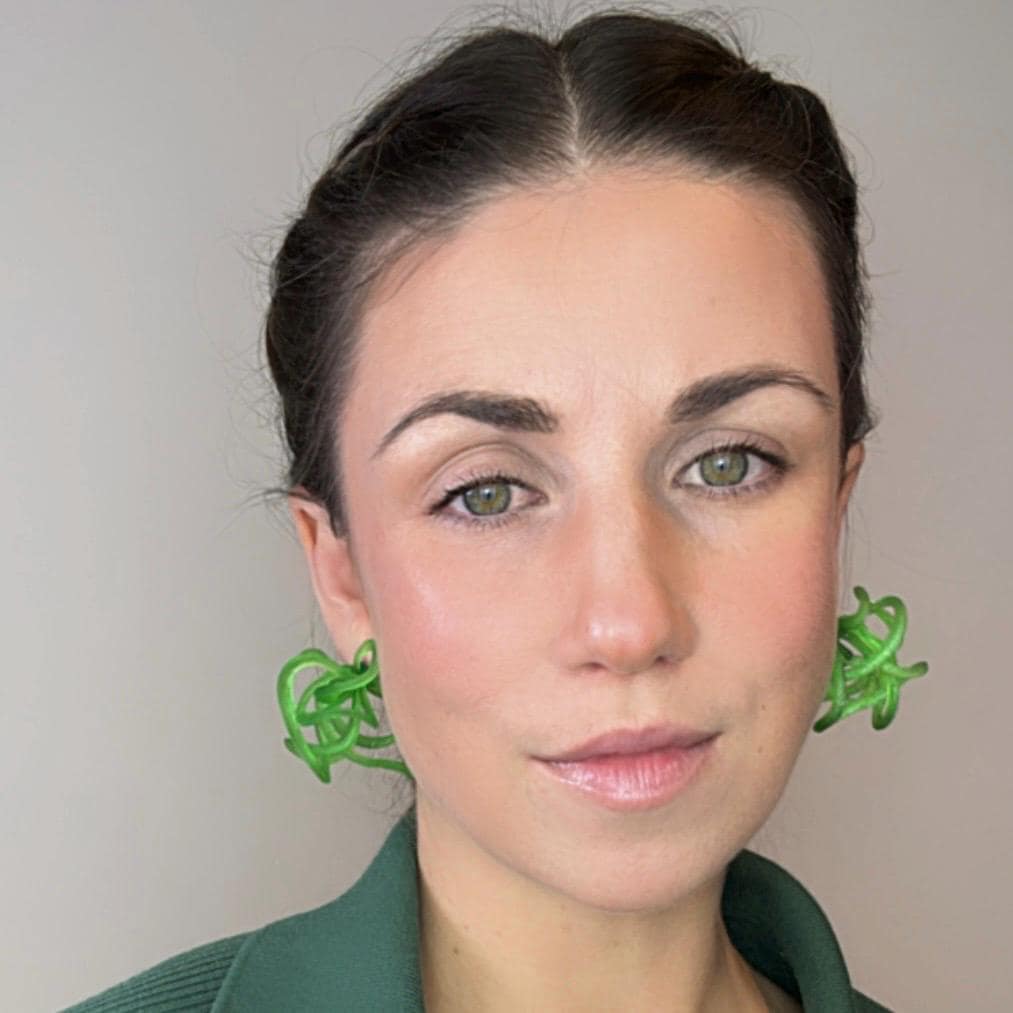 Person wearing green earrings against a plain background