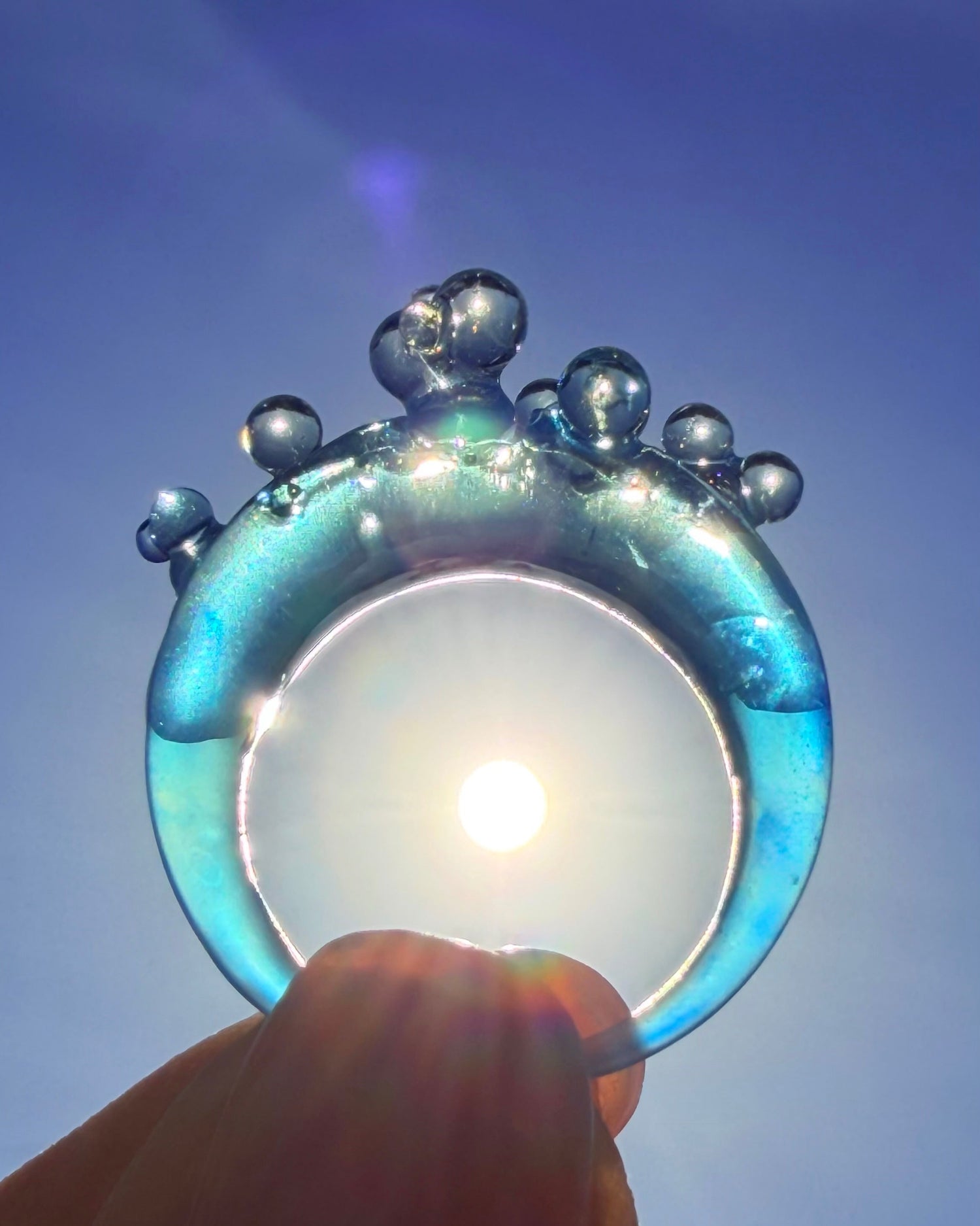 Transperent blue ring with bubble design held against a blue sky