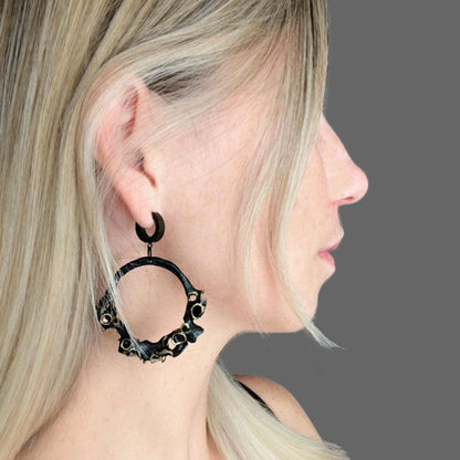 Person wearing a large black hoop earring with a grey background