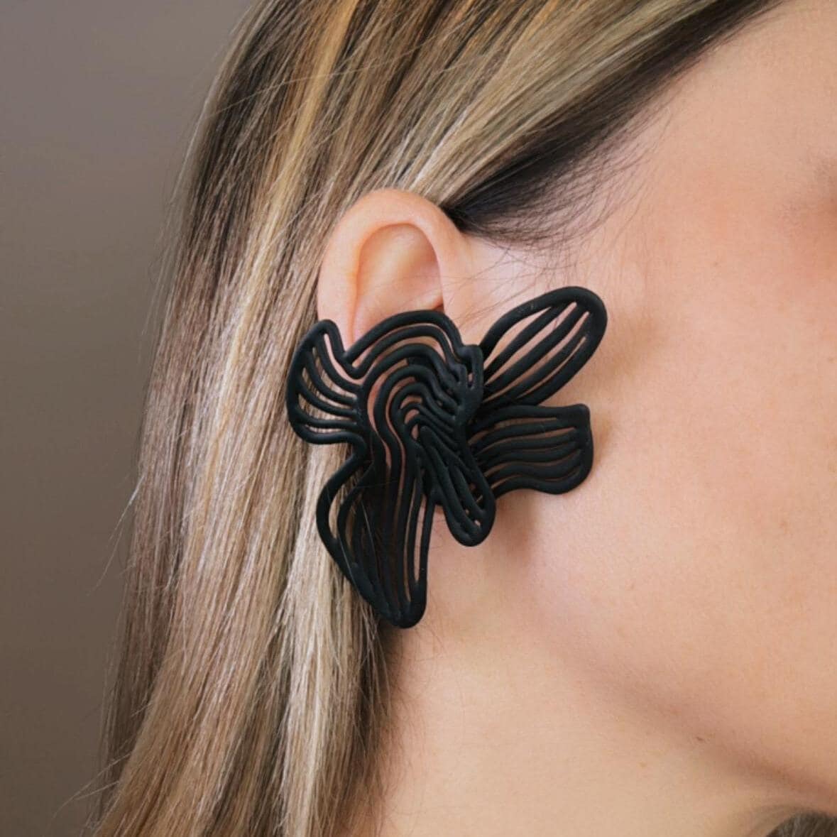 A person wearing a large black statement earring with a geometric design.