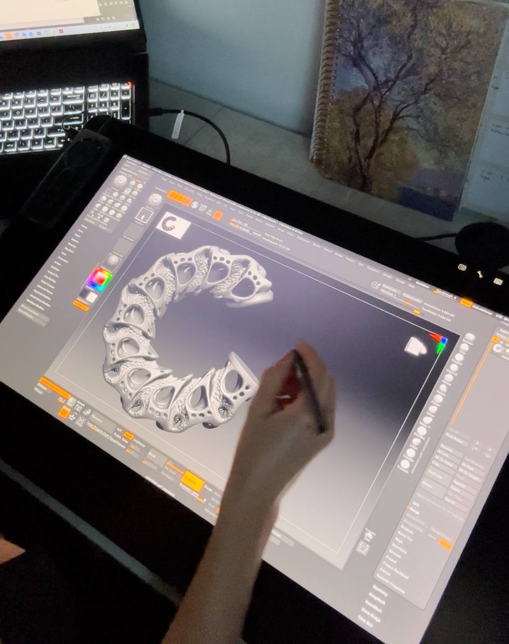 Person using a digital art tool on a large display with a computer setup in the background modeling 3d earrings