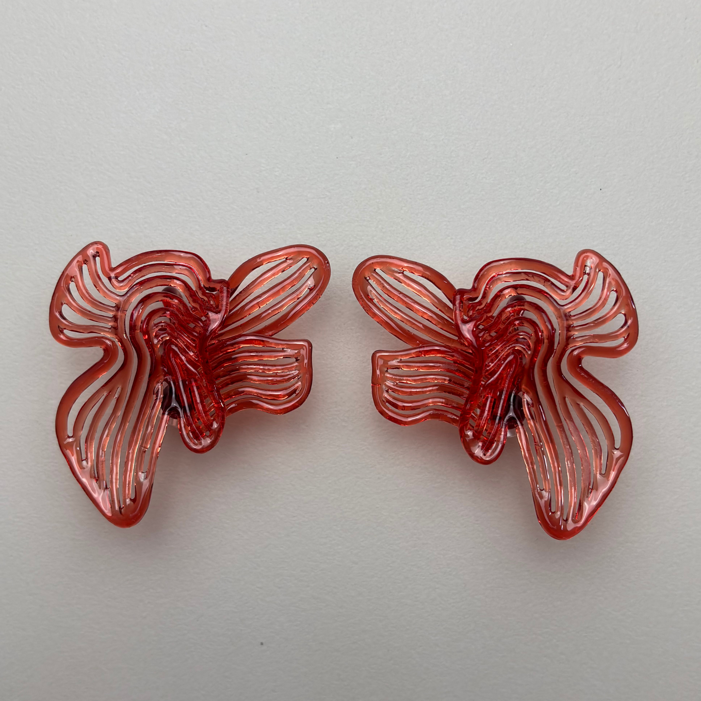 Two red butterfly-shaped 3d printed earring on a light gray background