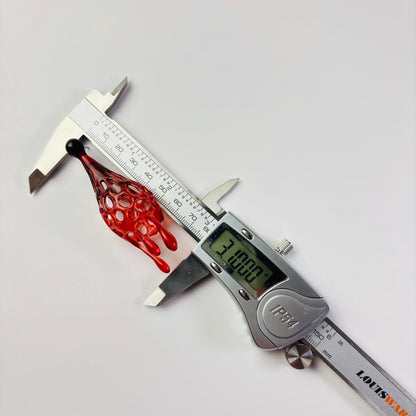 Digital caliper measuring a red and black 3d printed earrings on a white background