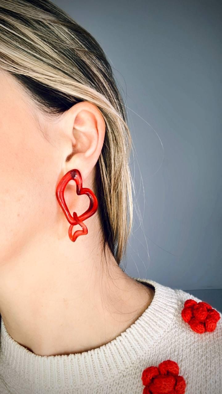 Person wearing red heart-shaped earrings with a neutral background.