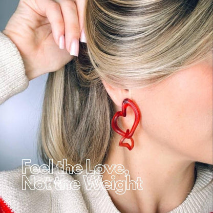 Person wearing red heart-shaped earrings with text overlay 'Feel the Love'.
