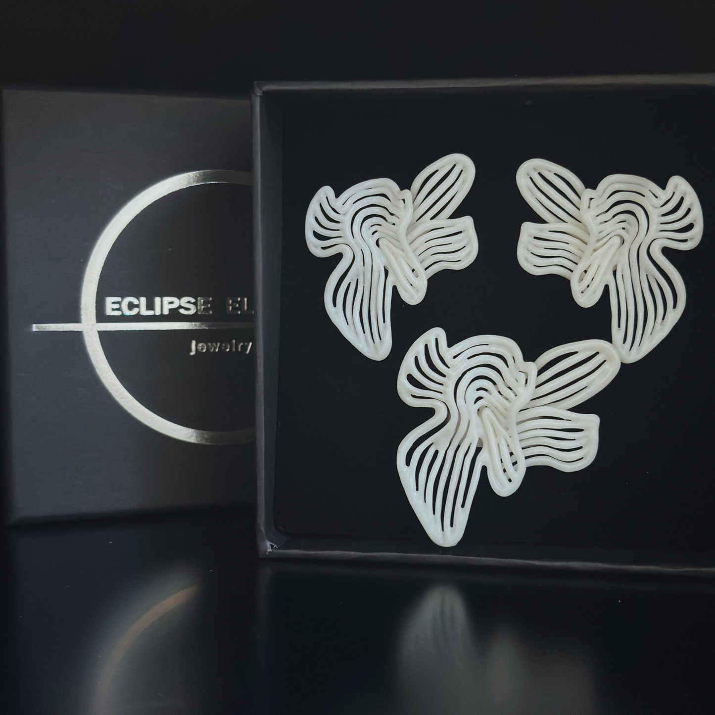 White sculptural floral earrings and ring set on black display box