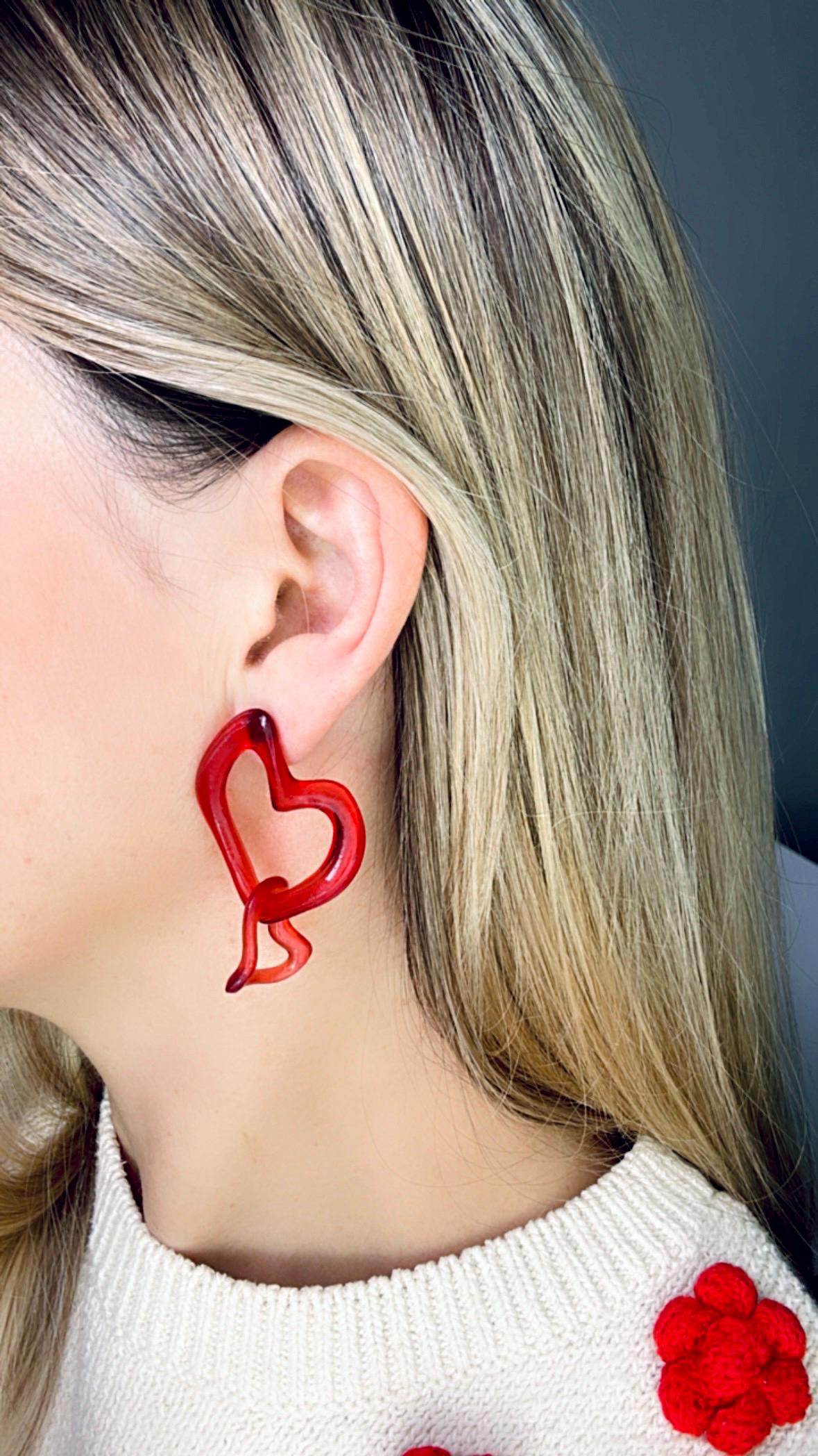 Red heart-shaped earring worn by a person with a neutral background.