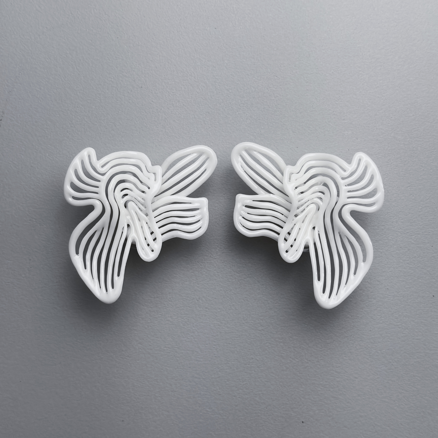 Two white floral-shaped 3d printed earrings on a gray background