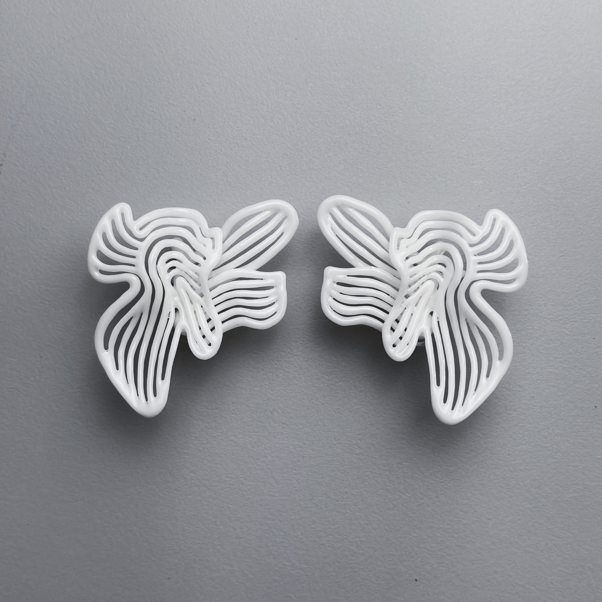 Two white floral-shaped 3d printed earrings on a gray background