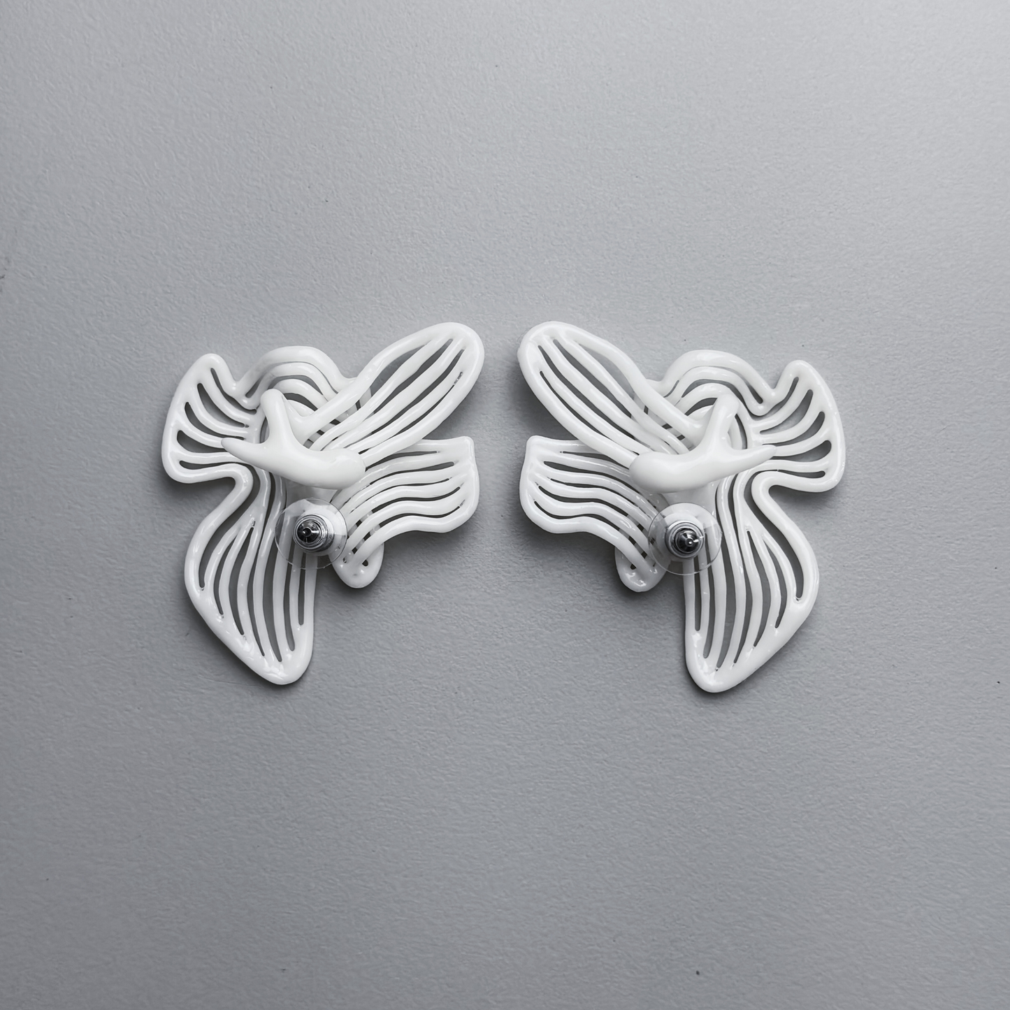 Pair of white white floral-shaped 3d printed earrings backs on a gray background